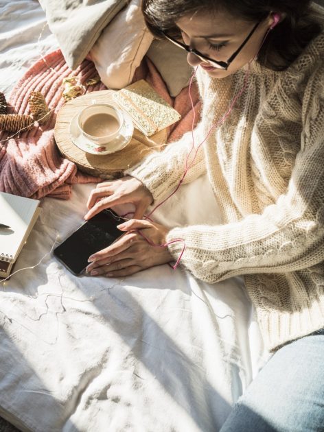 Woman surrounded by a phone, notebook, and coffee, focused on her phone — representing where daily attention and focus actually go