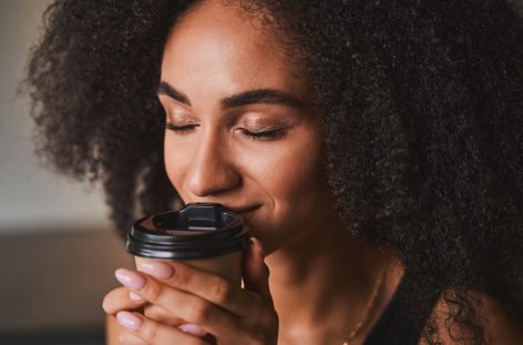 Close-up of a woman closing her eyes while holding a warm cup of coffee — a quiet moment before taking action