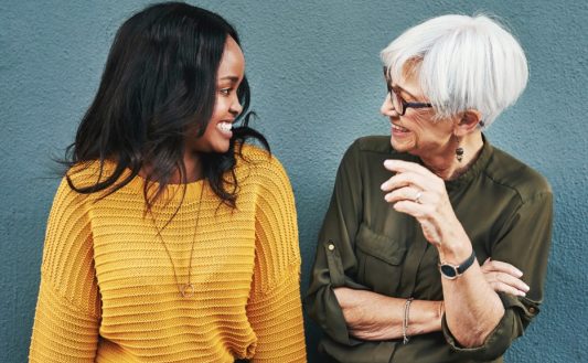 Two women of different generations laughing together in conversation against a wall